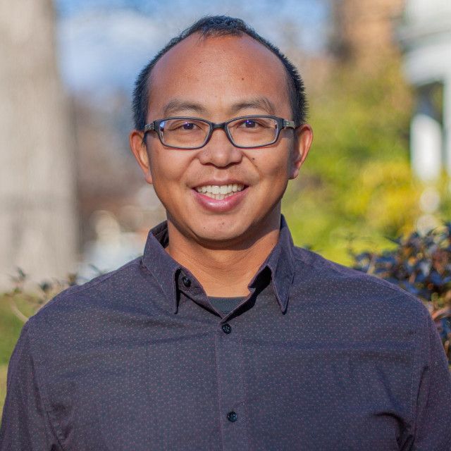 The image shows a man smiling outdoors.
