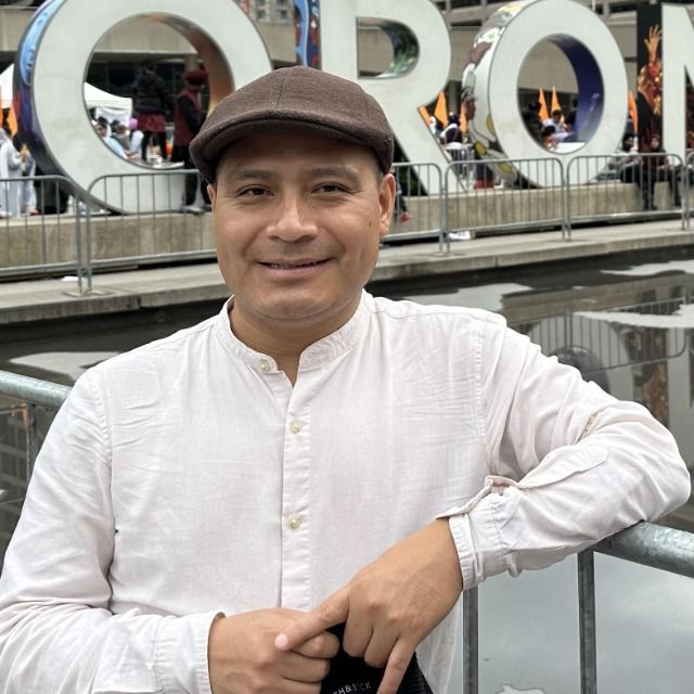 Man wearing white buttonup and brown hat is smiling.