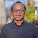 The image shows a man smiling outdoors.